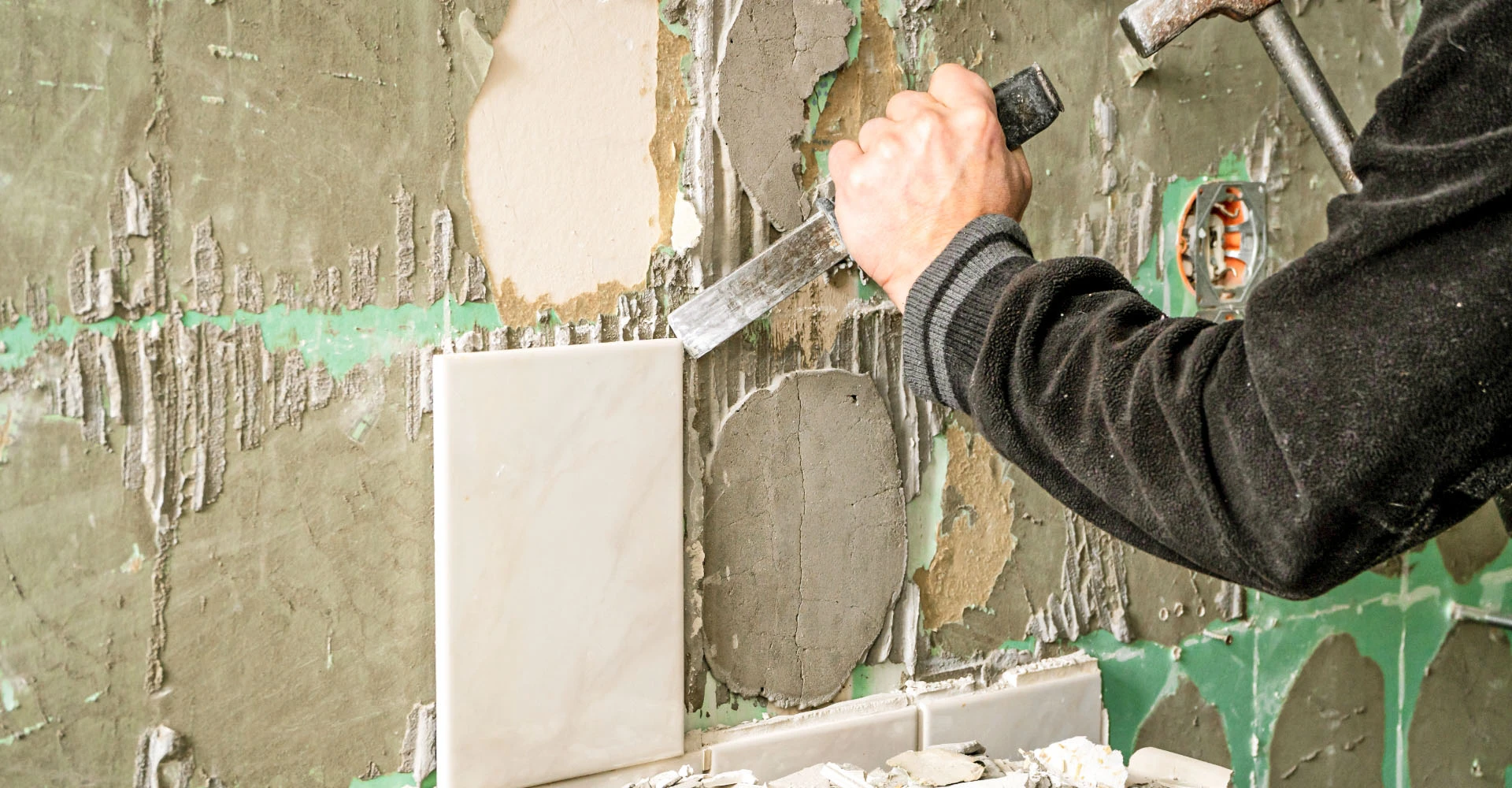 Eine Person entfernt Fliesen von einer Wand